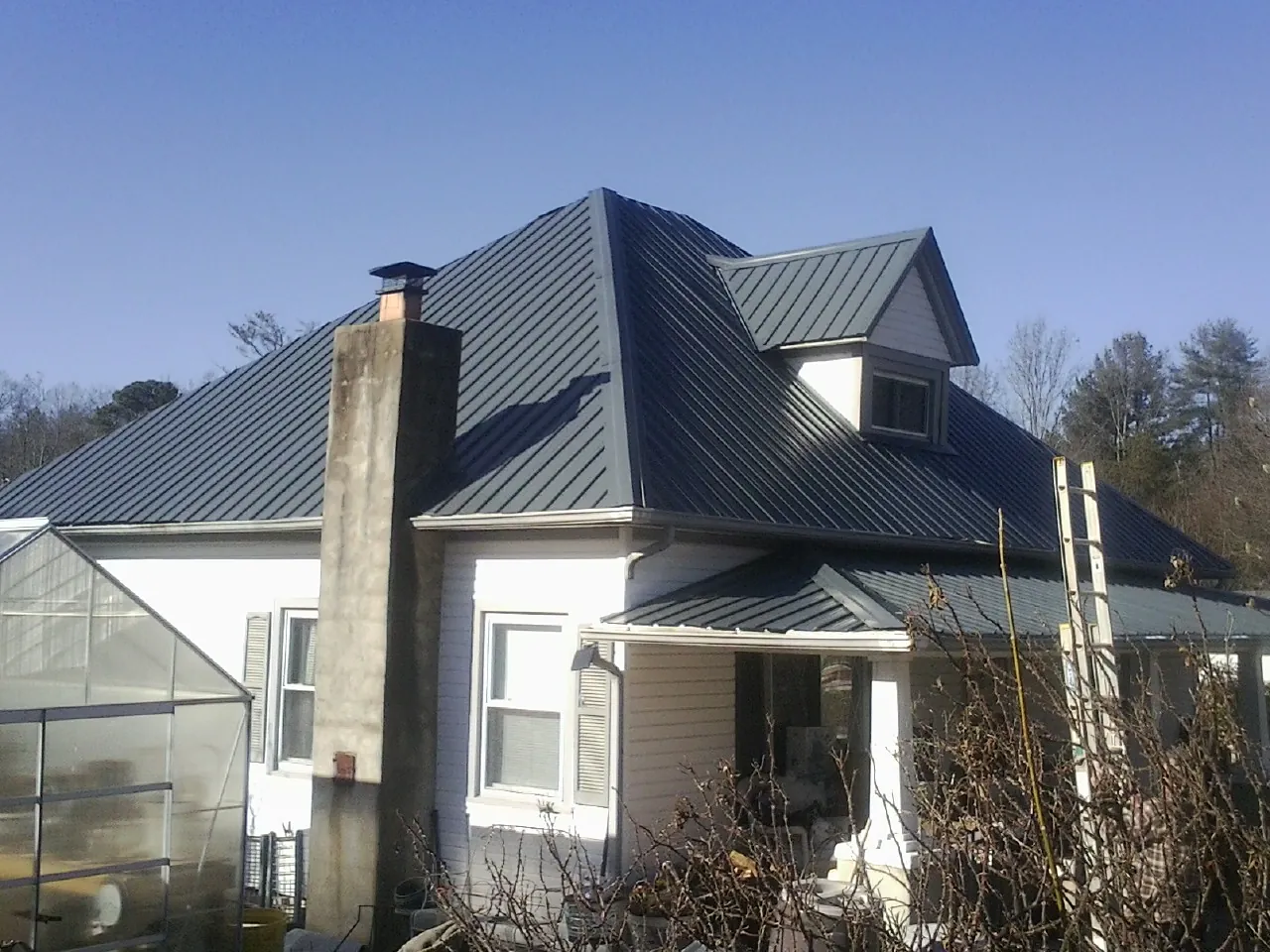 Dark blue standing seam metal roof on a white farmhouse with dormer — Slate & Tile Roof Repair by Roofing Brothers in Pittsville