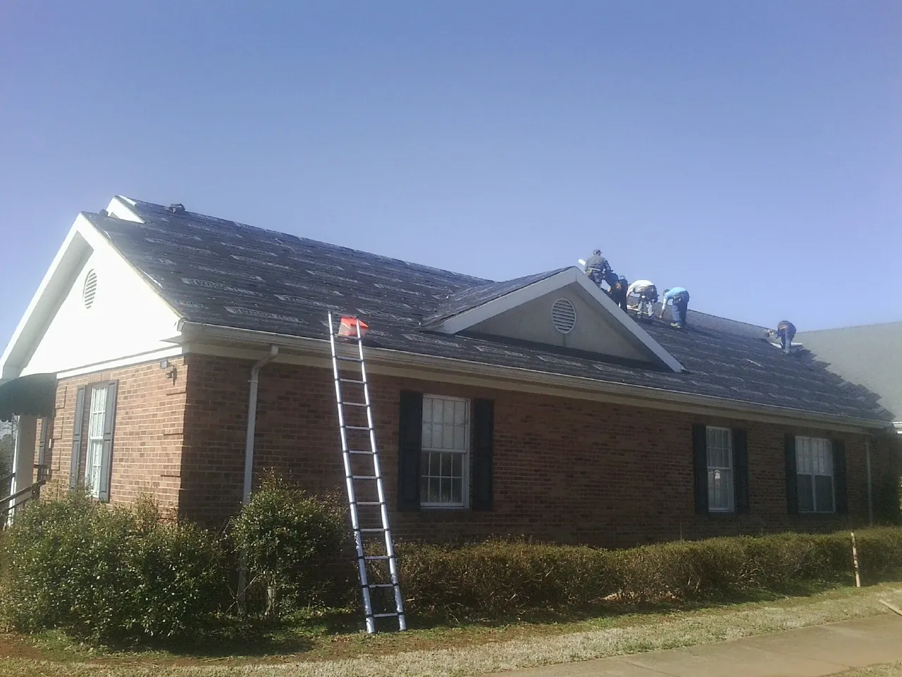 Crew tearing shingles off a brick ranch roof with a ladder set — Emergency Roof Repair work by our crew in Pittsville