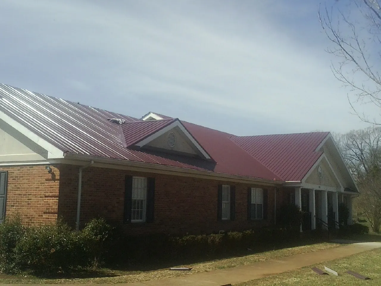 Red metal roof with gabled entries on a long brick building, from a Hail Damage Roof Repair job in Pittsville