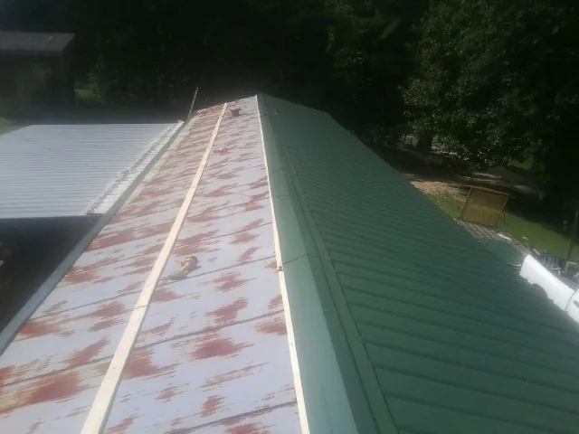 Old rusted panels beside newly installed green metal roofing — Wind Damage Roof Repair by Roofing Brothers in Pittsville