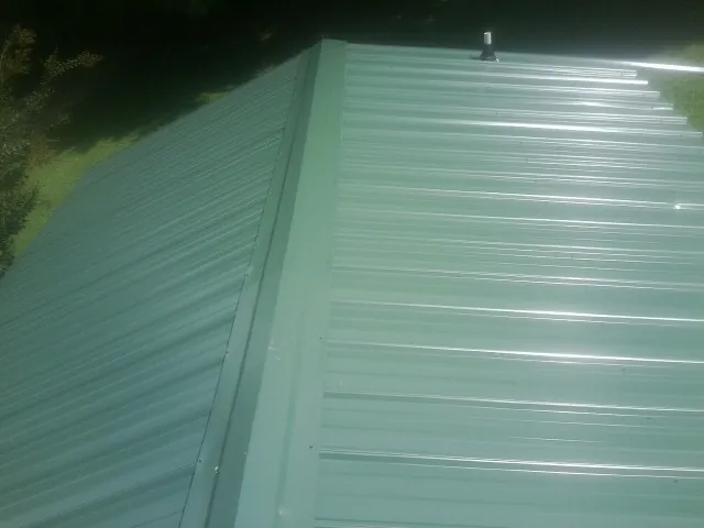 New green metal panels meeting at the ridge of a roof — Flat Roof Repair work by our crew in Pittsville