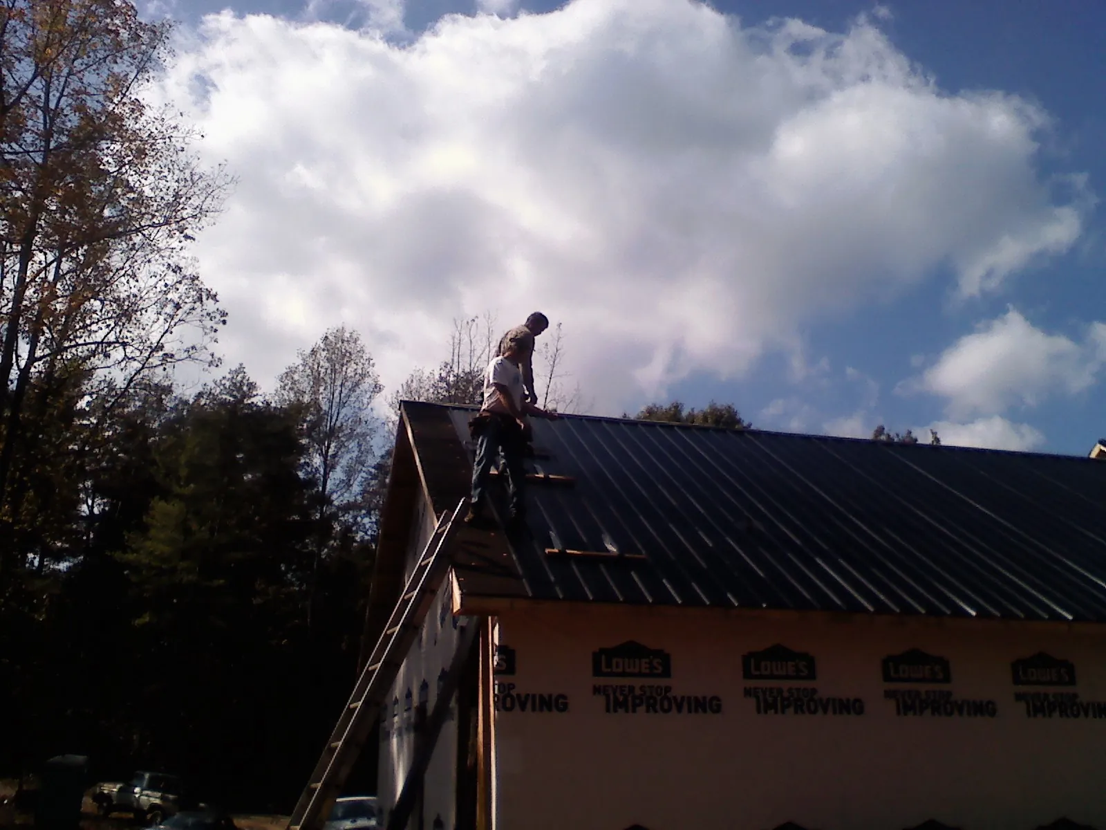 Roofer fastening dark metal panels high against a cloudy sky, from a Roof Inspection job in Pittsville