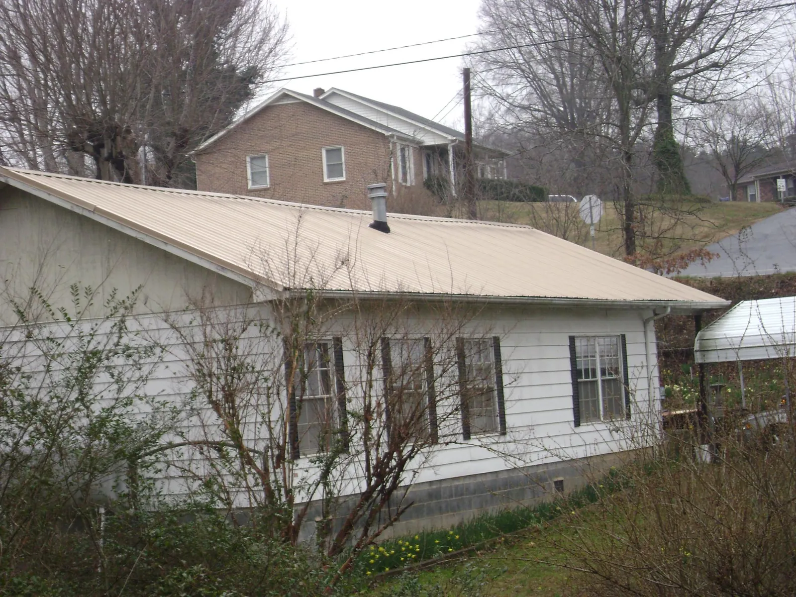 Tan metal roof on a white sided house set into a hillside — Commercial Roofing by Roofing Brothers in Pittsville