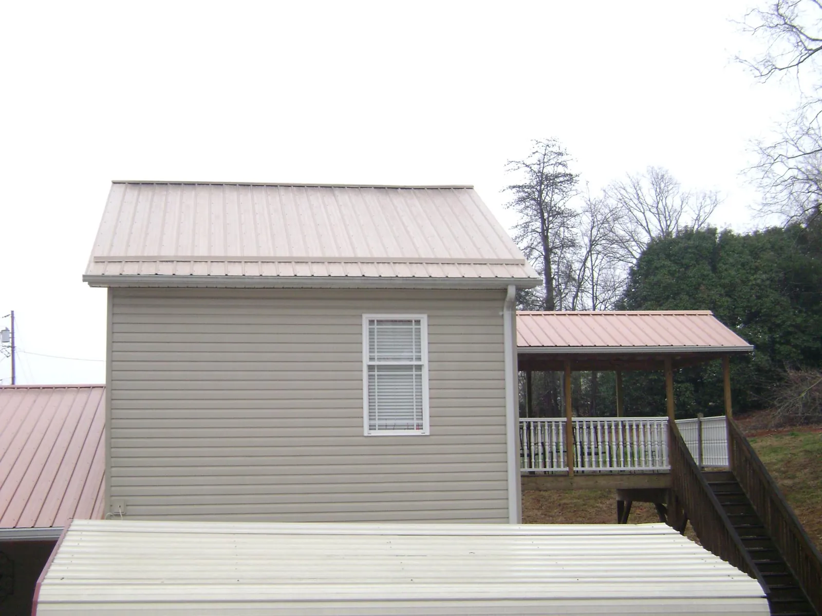 Tan metal roofs on a two story addition and attached porch, from a Roof Replacement job in Pittsville